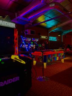 a room filled with arcade machines and neon colored lights on the ceiling, along with carpeted flooring