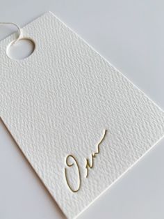 a close up of a tag on a white surface with the word q in gold ink