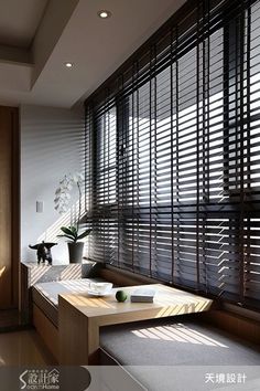 a living room filled with furniture and windows covered in blindes next to a plant