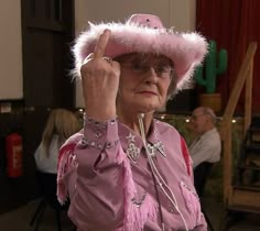 an older woman wearing a pink hat and holding her hand up to her head with other people in the background