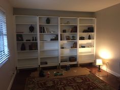 a living room filled with lots of white bookshelves next to a lamp on top of a rug