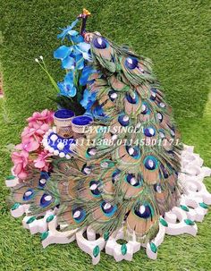 a peacock sitting on top of a lush green field next to pink and blue flowers