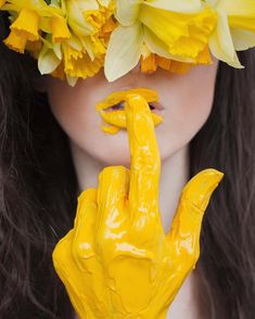 a woman with yellow paint on her face and hands holding flowers in front of her face