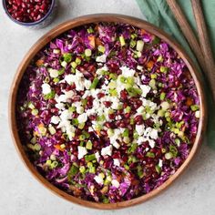 a wooden bowl filled with red cabbage and pomegranates next to two spoons