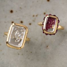 two gold rings with different colored stones on the top one has a square shaped diamond in it