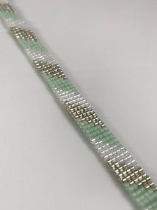 a green and white bracelet with silver beads on it's end, sitting on a table