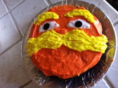 an orange frosted cake with googly eyes and a mustache