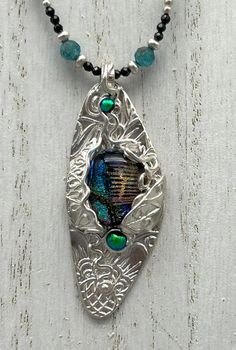 Asymmetrical Carnival, is an Original, Hand Made, One of a Kind, Fine Silver and Gemstone Art Necklace. Asymmetrical Carnival was created using an original, hand carved texture and fine silver metal clay shaped in a fun, asymmetrical shape! This unique pendant features a large, handmade, dichroic glass cabochon, and two smaller metallic blue glass cabochons.  All elements come together in a whimsical and artful one of a kind pendant! Asymmetrical Carnival is beaded using a "carnival" of colorful Unique Teardrop Jewelry With Artistic Design, Artisan Silver Jewelry With Czech Glass, Handmade Oval Czech Glass Jewelry, Silver Metal Clay, Art Necklace, Gemstone Art, Art Necklaces, Blue Apatite, Metal Clay