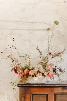 a vase filled with lots of flowers sitting on top of a wooden dresser next to a brick wall