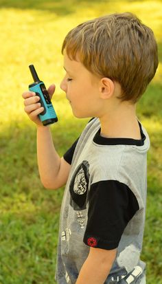 a young boy holding a cell phone in his right hand while standing on the grass