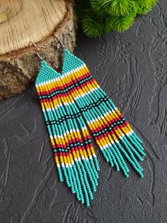 the multicolored beaded earrings are hanging from a piece of wood next to a tree