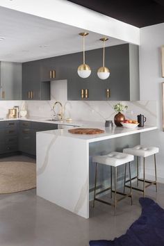 a modern kitchen with marble counter tops and gold pendant lights hanging from the ceiling over the island