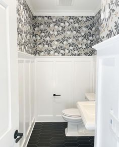 a white toilet sitting next to a sink in a bathroom under a window with floral wallpaper