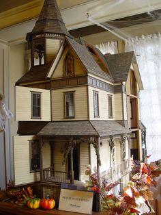 a doll house on display in front of a window with fall leaves and pumpkins