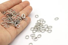 a hand holding a bunch of silver colored metal jump rings on top of a white table