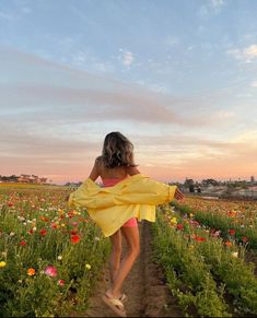 a woman in a yellow dress is walking through a flower field with her arms outstretched