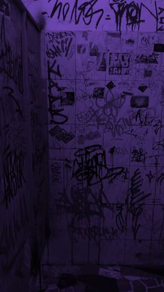 graffiti on the walls of a bathroom stall in purple hued lighting with black and white flooring