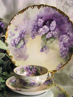 purple flowers are in the center of this tea cup and saucer