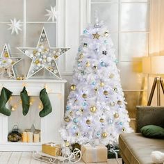 a white christmas tree decorated with gold and silver ornaments next to a fireplace in a living room