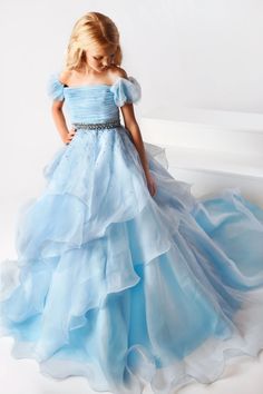 The Ava Presley 38025 Long Ruffle layer A Line Ballgown is designed for girls' pageant wear, offering classic style and sophistication. Its off-the-shoulder design features a puff sleeve, ruffle layer and detailed craftsmanship for an elegant look. Made of soft and durable fabric, it offers superior comfort and long-lasting wear.  Sizes: 2-16  Colors: Light Blue, Coral, White Waterfall Dress, Pageant Wear, Dress Puff Sleeve, Girls Pageant Dresses, Girls Pink Dress, Ball Gown Skirt, Pageant Gowns, Beaded Bodice, Pageant Dress