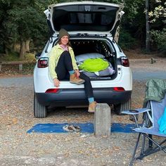 a woman sitting in the back of a white van with her camping gear set up