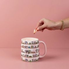 a person is holding a coffee mug with books on it and the cup has a pencil sticking out of it