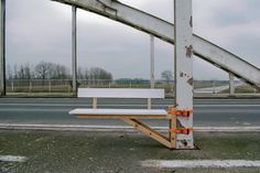 a white bench sitting on the side of a road next to a metal pole with an orange stripe