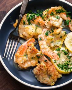 a blue plate topped with shrimp and lemons on top of a wooden table next to a fork