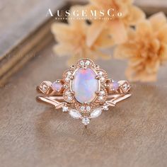 an opal and diamond ring sits on top of a wooden table next to flowers