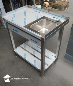 a stainless steel sink on wheels with blue tape around the bottom and side shelves for storage