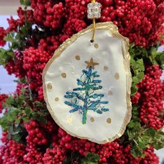 a christmas ornament hanging from a tree with red berries on the branches and gold dots around it