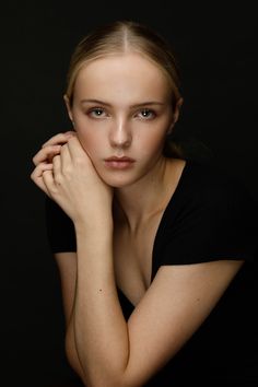 a woman posing with her hand on her chin and looking at the camera while wearing a black shirt