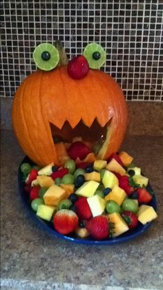 a plate full of fruit with a pumpkin carved into the top and eyes on it