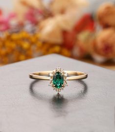 an emerald colored ring sitting on top of a wooden table with flowers in the background