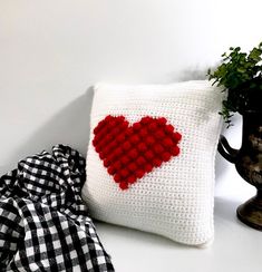 a crocheted pillow with a red heart on it next to a potted plant