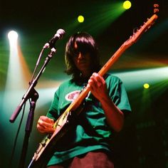 a man playing an electric guitar in front of a microphone and some green spotlights