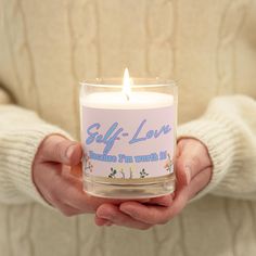 a person holding a candle in their hands with the words self love written on it