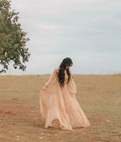 a woman standing in the middle of a field wearing a long, flowing peach dress