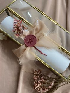 a white candle in a glass box with a ribbon around it and some dried flowers