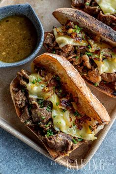 two sandwiches with meat and cheese are on a plate next to a bowl of dipping sauce