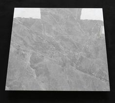 a square marble tile on a black surface with white border around the edges and gray veining