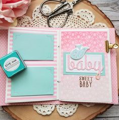 a baby scrapbook is open on a wooden table with scissors and pink flowers in the background