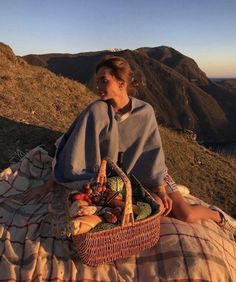 a woman sitting on top of a hill next to a basket filled with food