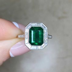 A halo engagement ring featuring a 2.66 carat emerald-cut natural green emerald. The emerald is bezel-set in platinum and surrounded by a halo of baguette cut diamonds with a total weight of 0.73 carats. Round brilliant cut diamonds weighing 0.14 carats total adorn the shoulders. The mounting is decorated with an openwork under-gallery and fine milgrain. This ring is handcrafted in platinum.
The measurements of this ring including the diamond halo are approximately 13.78mm x 12.18mm.
The current Luxury Octagon Emerald Ring With Diamond Accents, Emerald Baguette Cut Ring With Bezel Setting, Bezel Set Baguette Cut Emerald Ring, Baguette Cut Emerald Ring With Bezel Setting, Baguette Cut Bezel Set Emerald Ring, Octagon Emerald Ring With Halo Setting, Gia Certified Emerald Cut Halo Ring, Octagon White Gold Emerald Ring With Halo Setting, White Gold Octagon Emerald Ring With Halo Setting