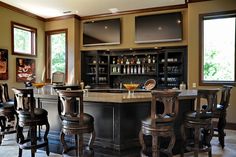 an elegant home bar with stools in the middle and television screens on the wall