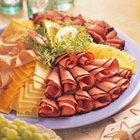 a platter filled with meat and cheeses on top of a table next to grapes