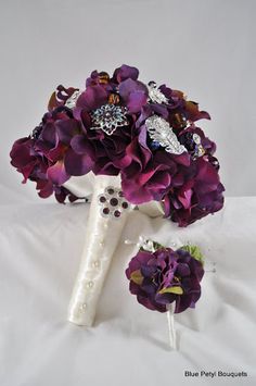 a bridal bouquet with purple flowers and brooches on a white cloth background