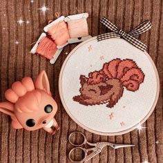 a cross - stitch project with scissors, yarn and a small toy on a table