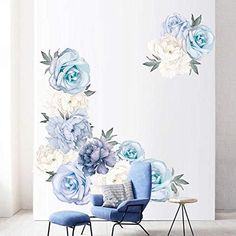 a blue chair sitting in front of a white wall with flowers on it and two small tables