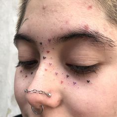 a woman with black spots on her face and nose piercings is looking at the camera